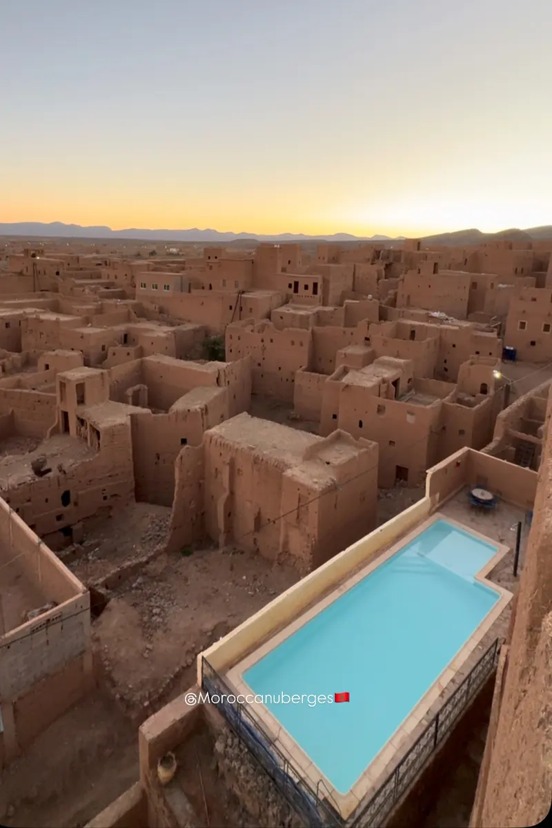 Vue sur un ksar en pisé au coucher du soleil, piscine au premier plan