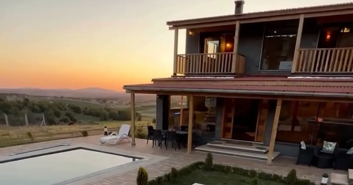 Chalet en bois à véranda et piscine, au coucher du soleil sur la campagne vallonnée