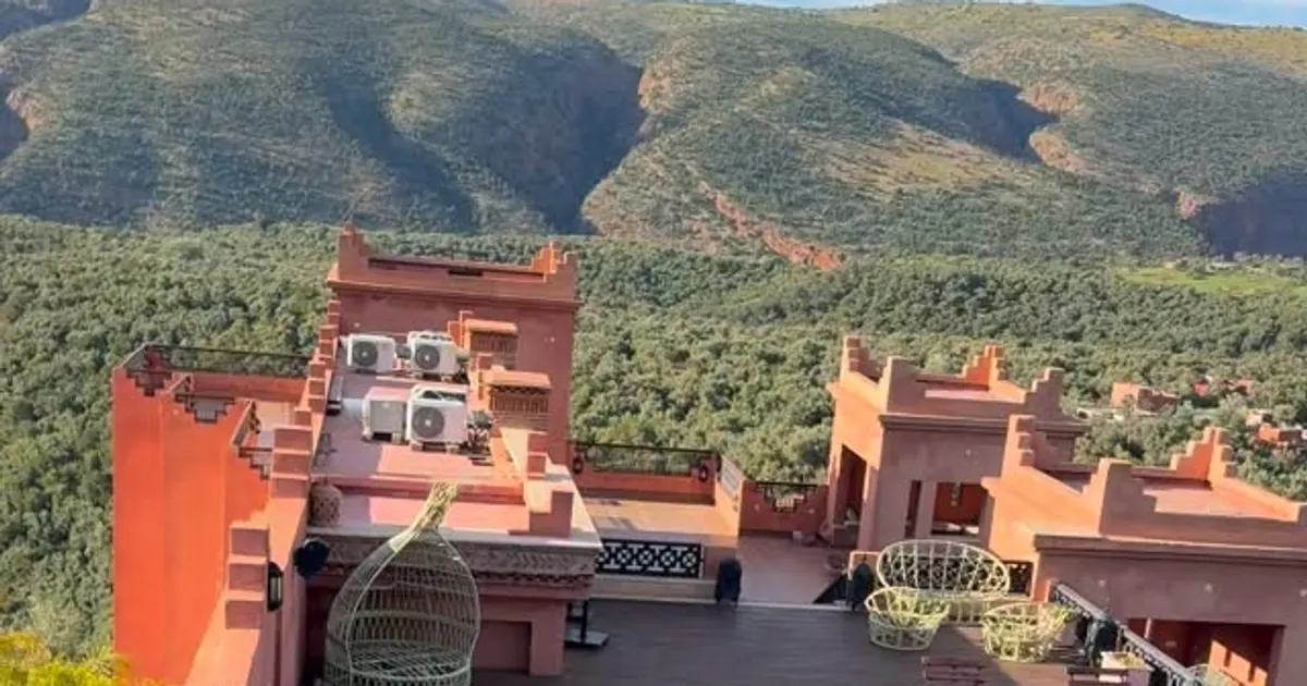 Toits-terrasses en ocre d'un hôtel d'Ouzoud, avec fauteuils en rotin, face aux collines boisées de la vallée